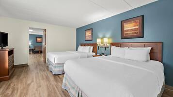 A hotel room with two beds, a TV, a desk, and a bathroom visible through an open door.