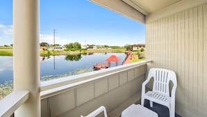 Un balcon donnant sur un plan d’eau, un parasol rouge et des chaises en plastique blanches.