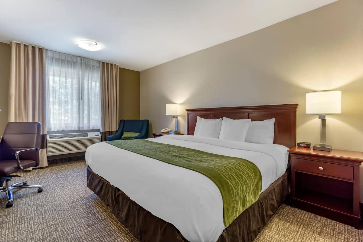 A hotel room with a large bed, a desk with a chair, a window with curtains, and two bedside lamps.