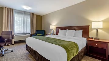 Habitación de hotel con una cama grande, un escritorio con silla, una ventana con cortinas y dos lámparas de noche.