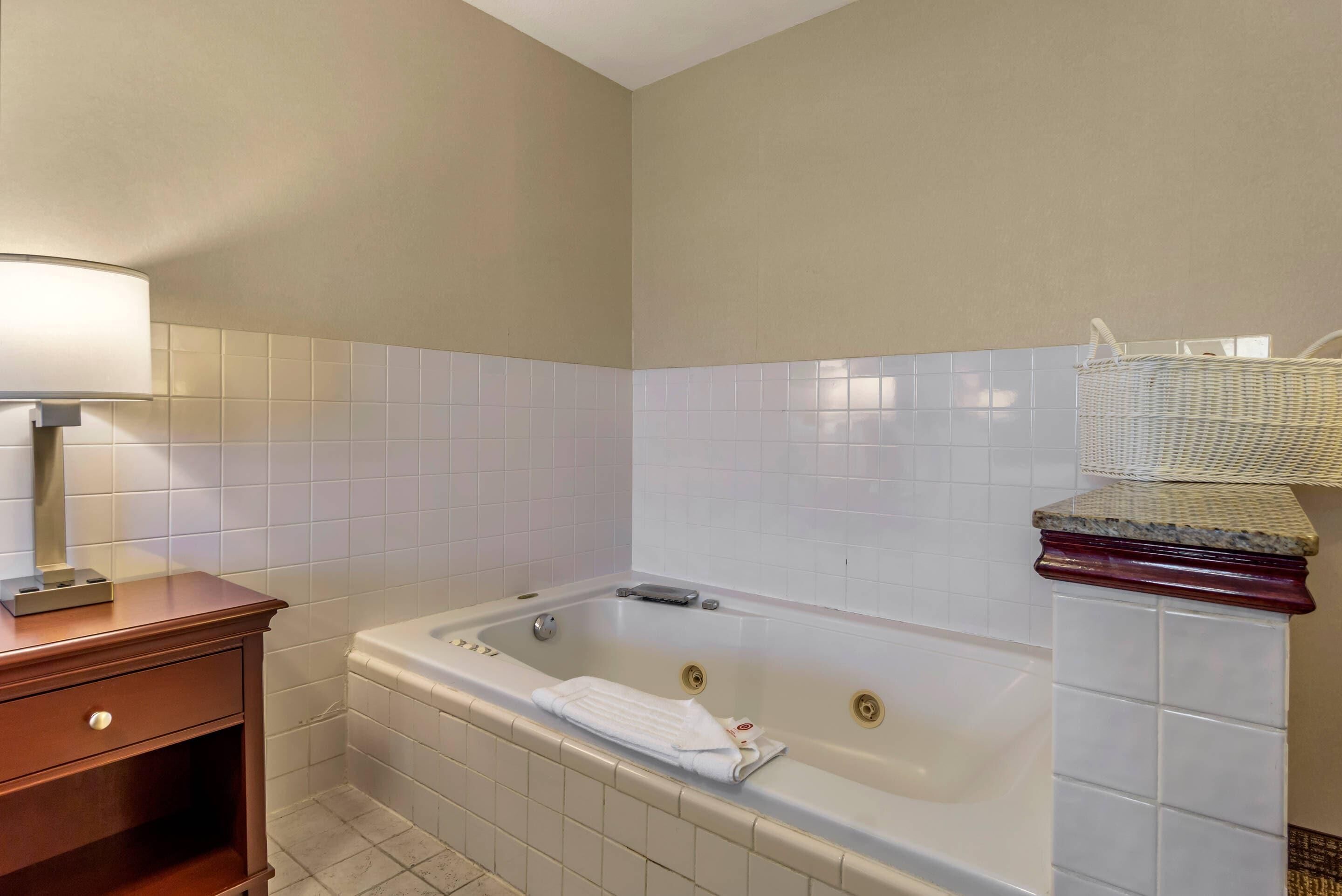 Un bagno con una vasca, un comodino in legno e una parete rivestita di piastrelle bianche.
