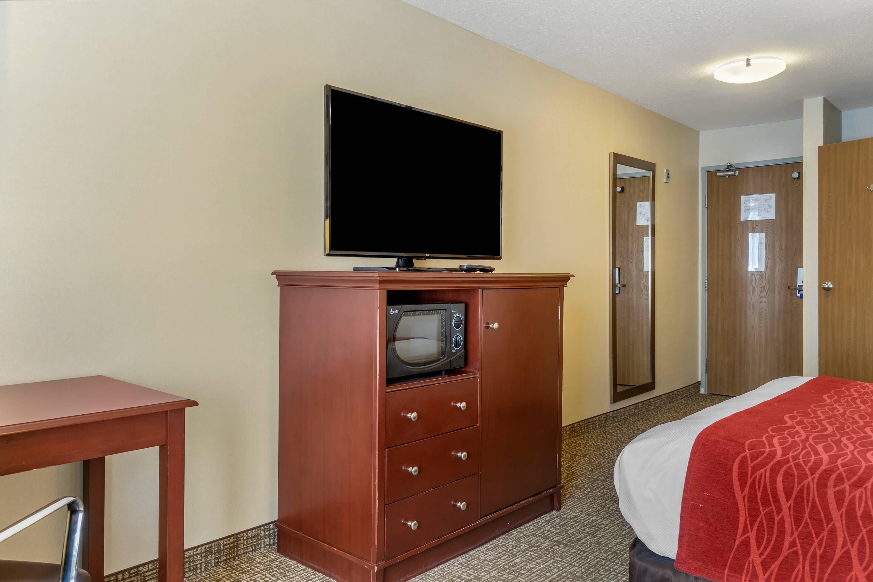 A hotel room with a bed, a TV, a microwave, a wooden cabinet, and a door.