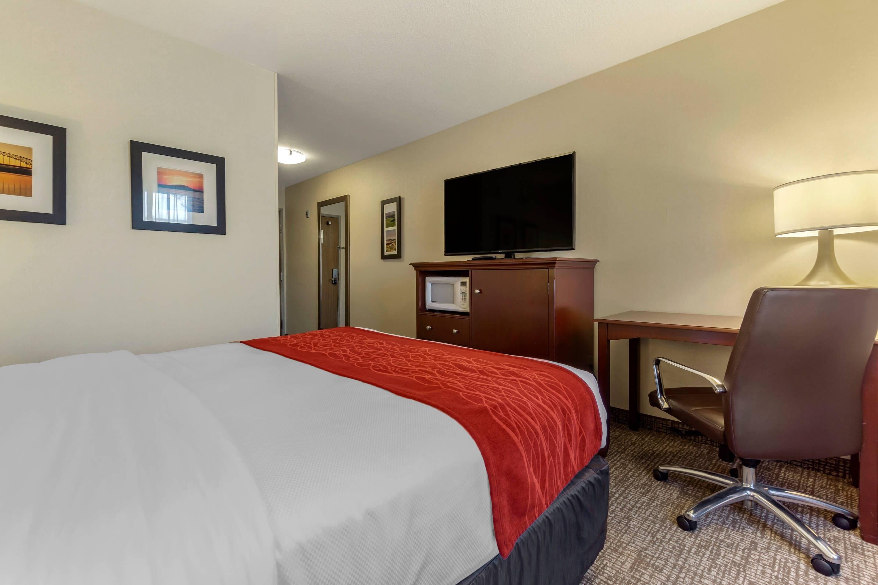 Una habitación de hotel con cama, escritorio, silla, televisor y lámpara.