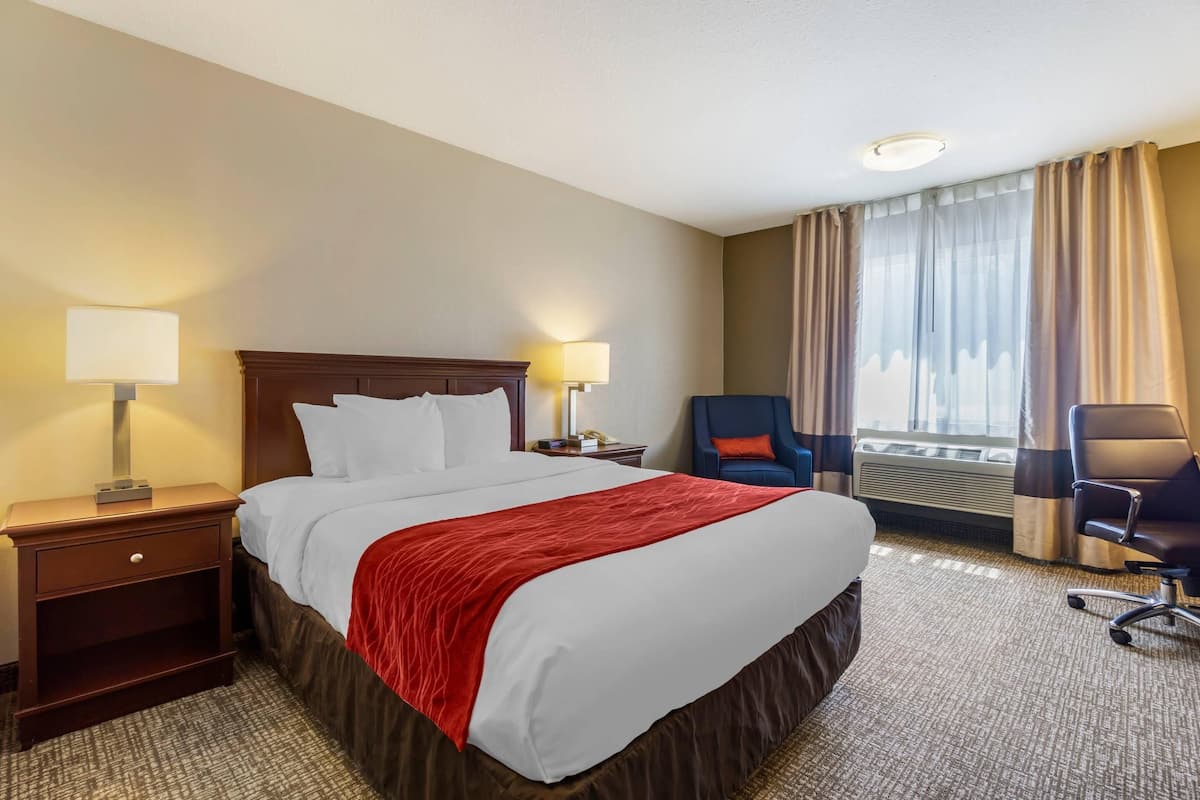 A hotel room with a large bed, two bedside tables with lamps, a chair, and a window with curtains.