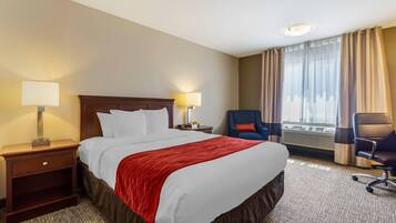 Een hotelkamer met een groot bed, twee nachtkastjes met lampen, een stoel en een raam met gordijnen.