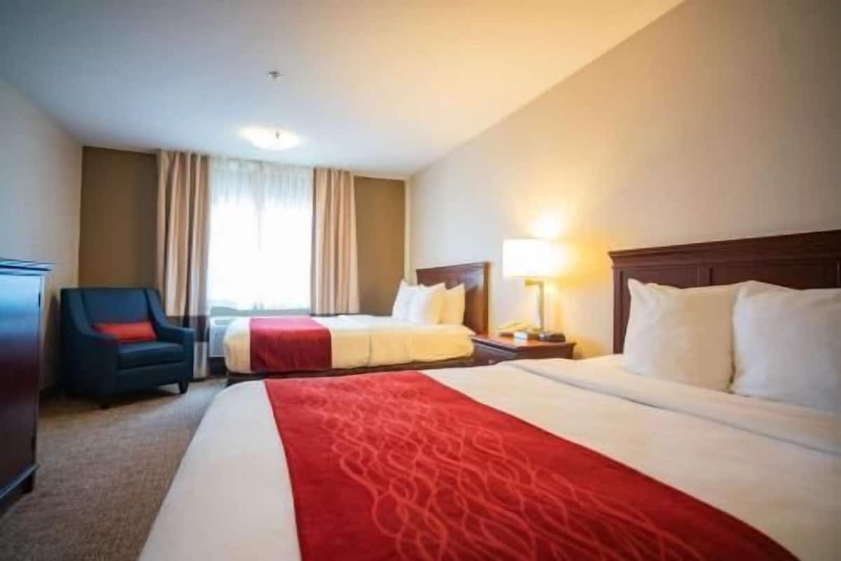 A hotel room with two beds, a desk, a chair, and a window with curtains.