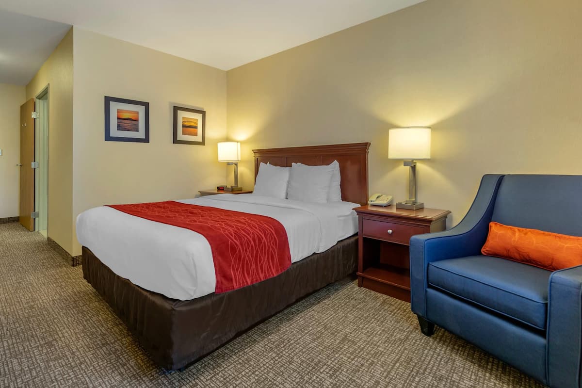 A hotel room with a large bed, two bedside lamps, a blue armchair, and two framed pictures on the wall.