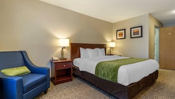 A hotel room with a large bed, a blue armchair, a nightstand, two wall-mounted lamps, and two framed pictures on the wall.