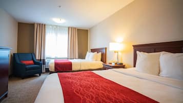 A hotel room with two beds, a chair, a desk, and a lamp.