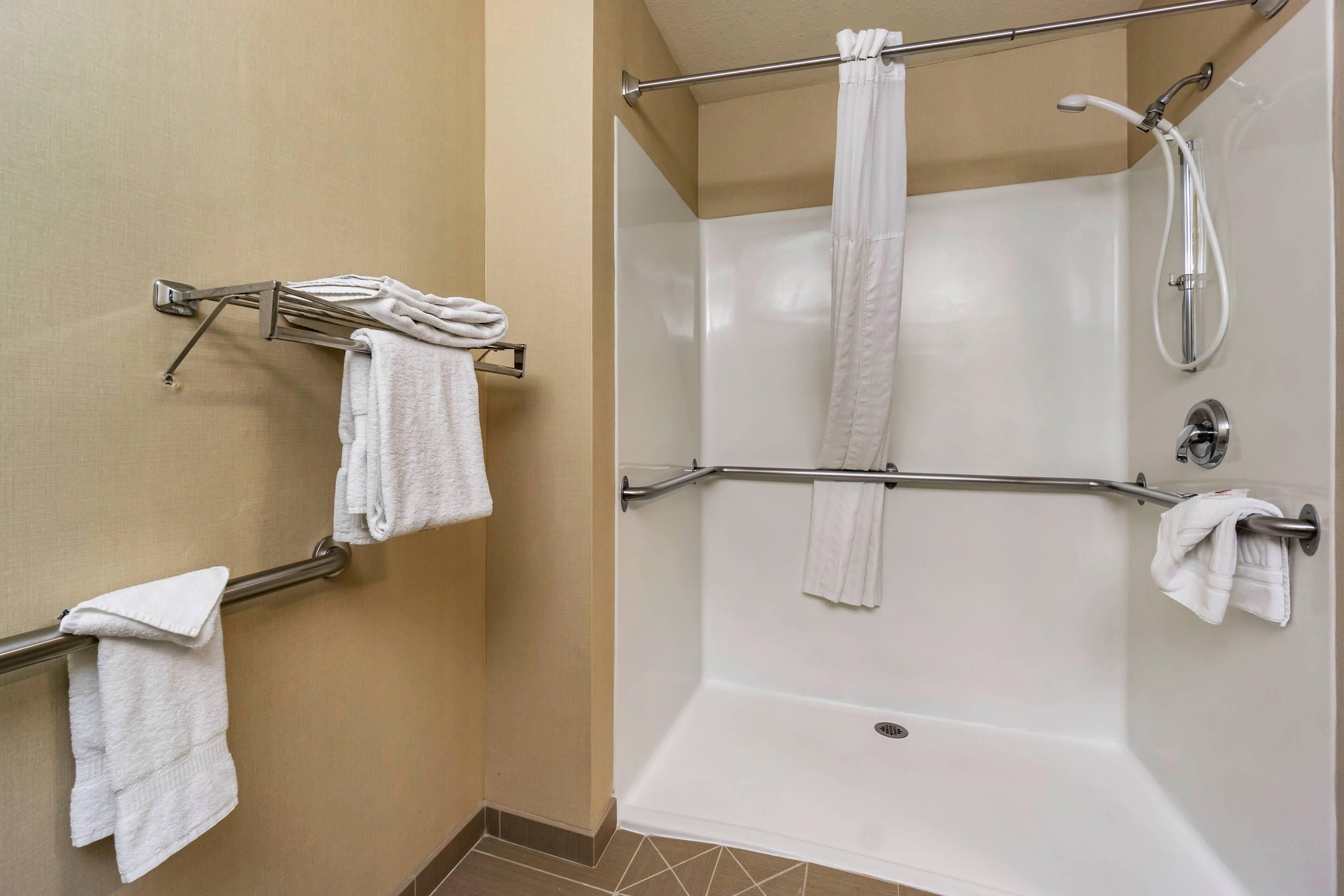 A shower area with a glass door, a metal grab bar, and white towels hanging on the wall.