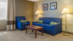 A hotel room with a blue sofa, a matching armchair, a wooden coffee table, two wall-mounted lamps, and a framed picture on the wall. - Comfort Inn Kennewick Richland (Kennewick)