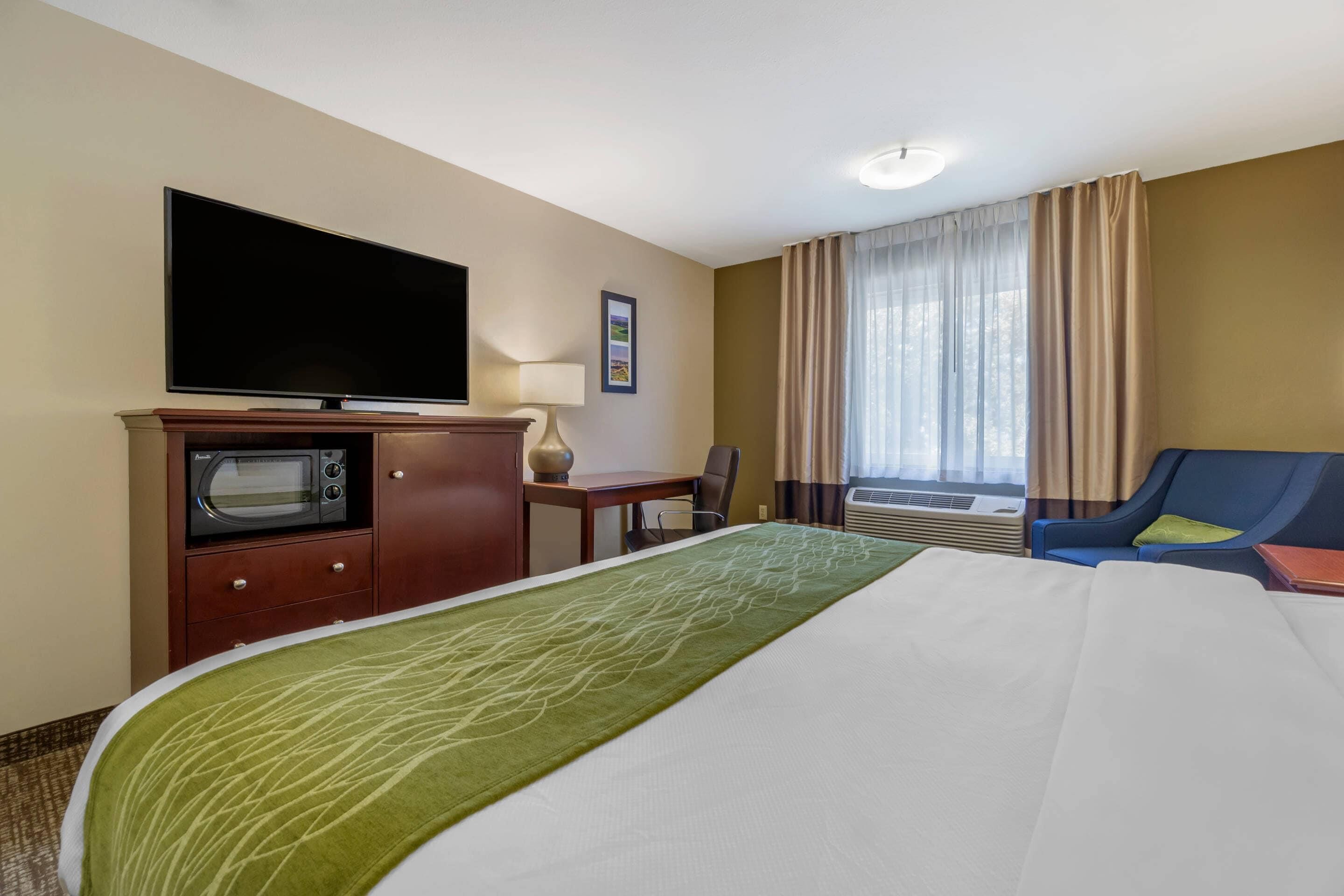 Une chambre d’hôtel équipée d’un lit, d’une télévision, d’un bureau, d’une chaise et d’une fenêtre avec des rideaux.