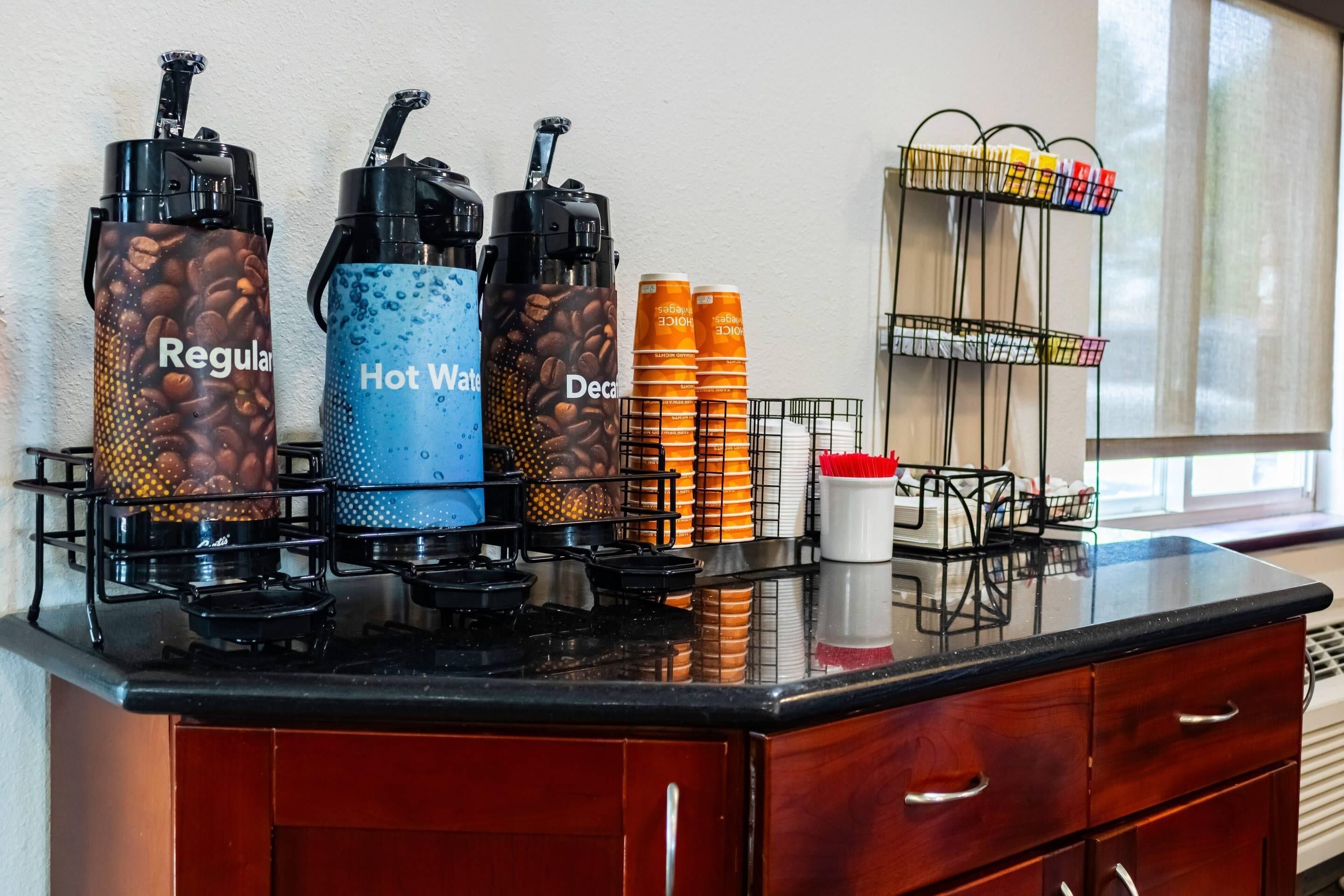 A kitchen area with coffee dispensers labeled "Regular," "Hot Water," and "Decaf." There are stacked cups and a coffee machine on the counter.