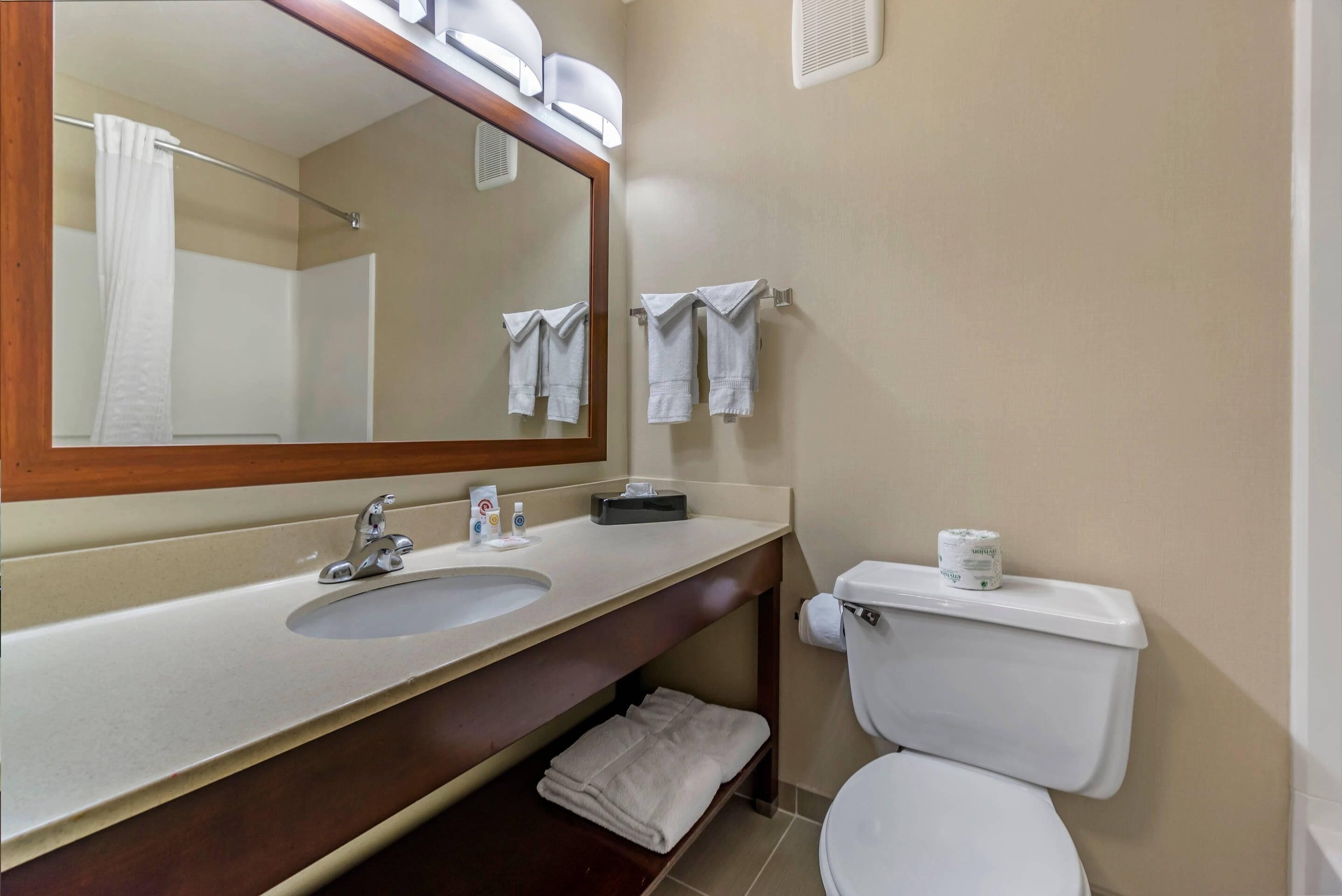 A bathroom with a sink, mirror, towel rack, toilet, and a towel folded on the floor.
