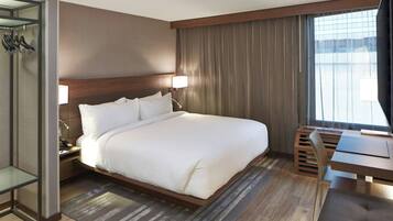 A modern hotel room with a large bed, bedside tables, a desk, and a window with curtains.
