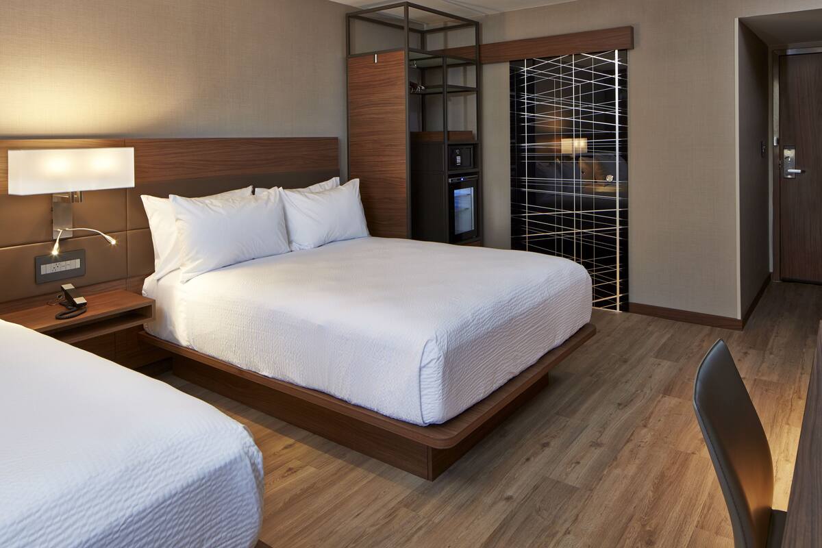 A hotel room with a large bed, a nightstand with a lamp, a wardrobe, and a desk with a chair.