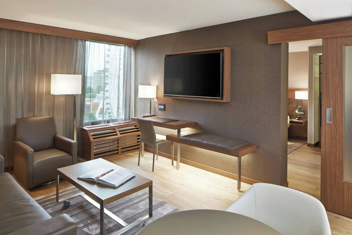 A modern hotel room with a large flat-screen TV, a sofa, a dining table, and a chair.
