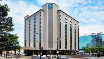 Un hotel moderno con el logotipo destacado de AC, varios pisos y un edificio de vidrio reflectante aledaño.