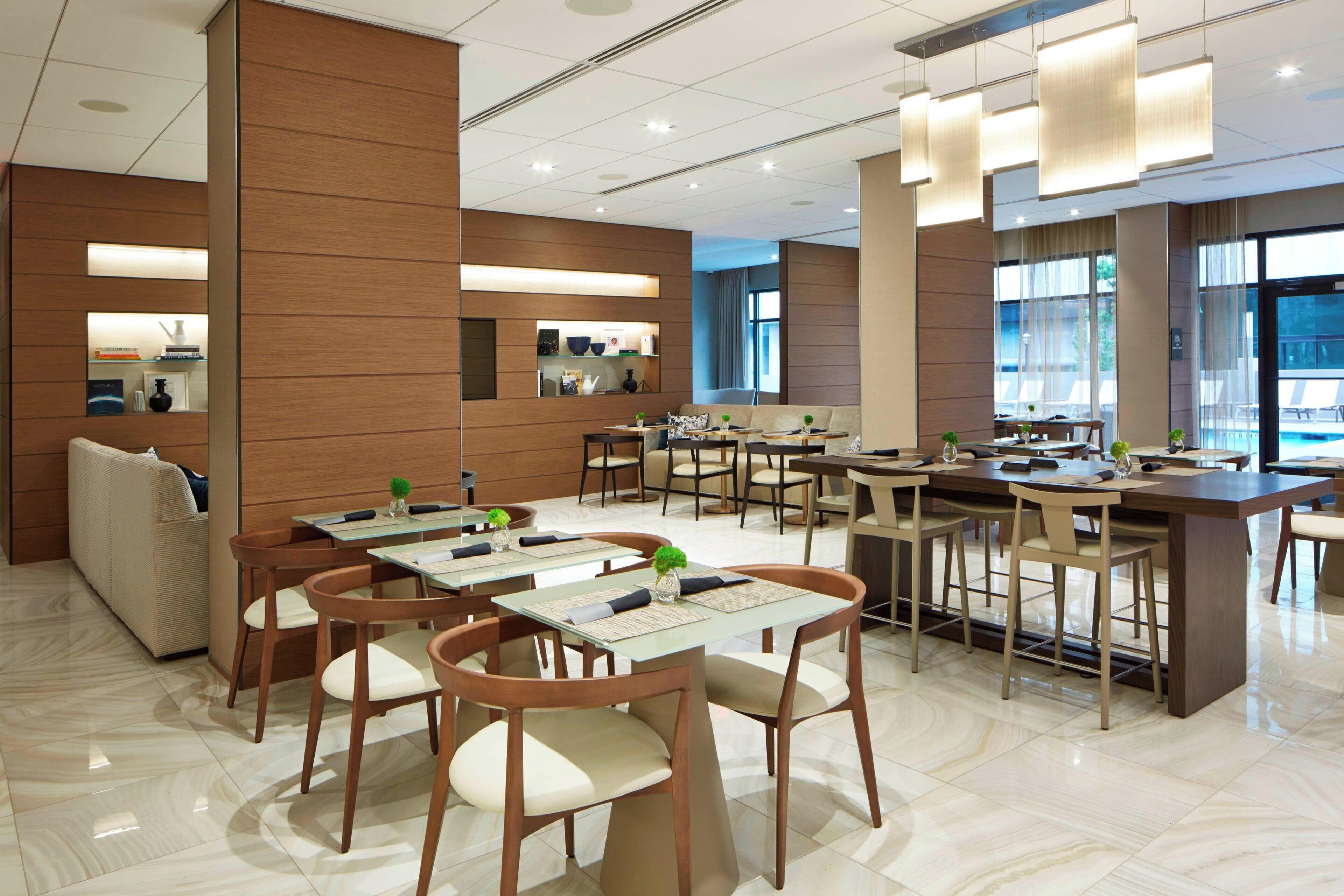 A modern dining area with multiple tables and chairs, a sofa, and a pool view.
