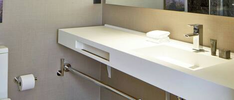 A modern bathroom with a white sink, a mirror, a toilet, and a trash can.