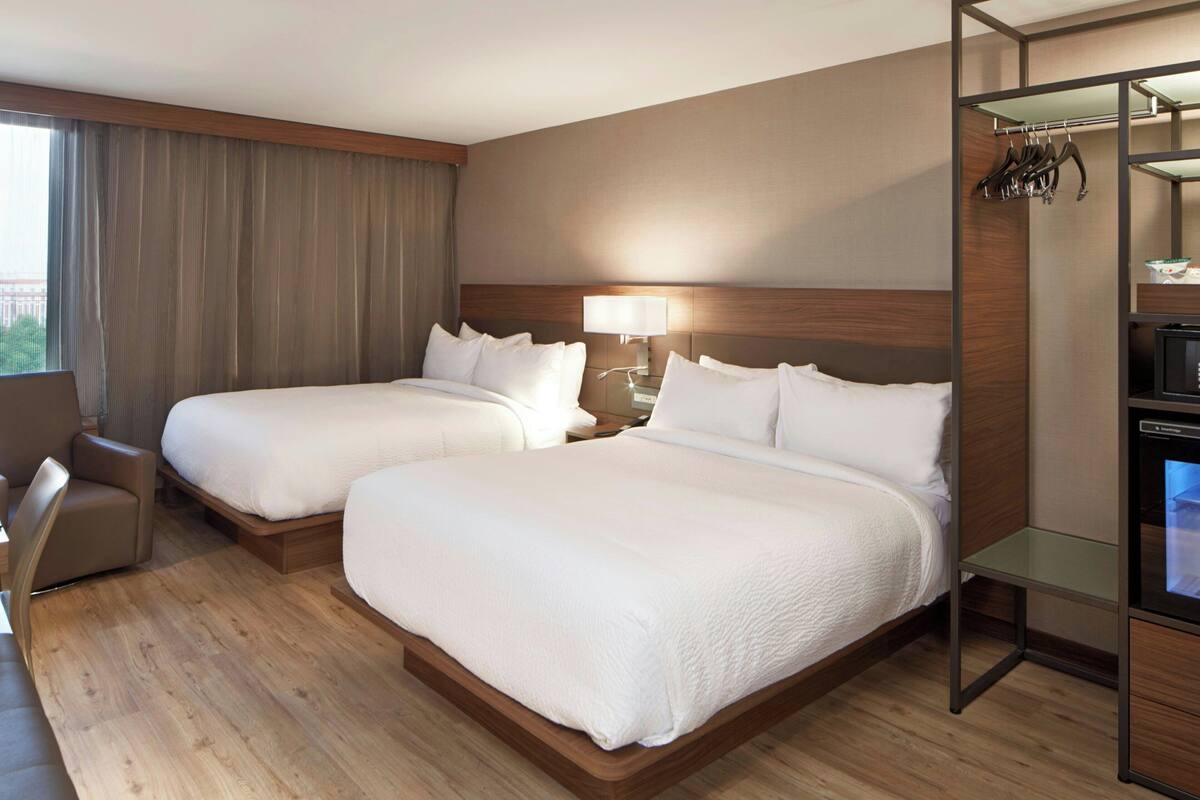 A hotel room with two beds, a desk, a chair, a TV, and a wardrobe.