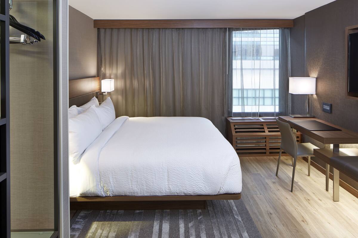 A modern hotel room with a large bed, a desk, and a television.