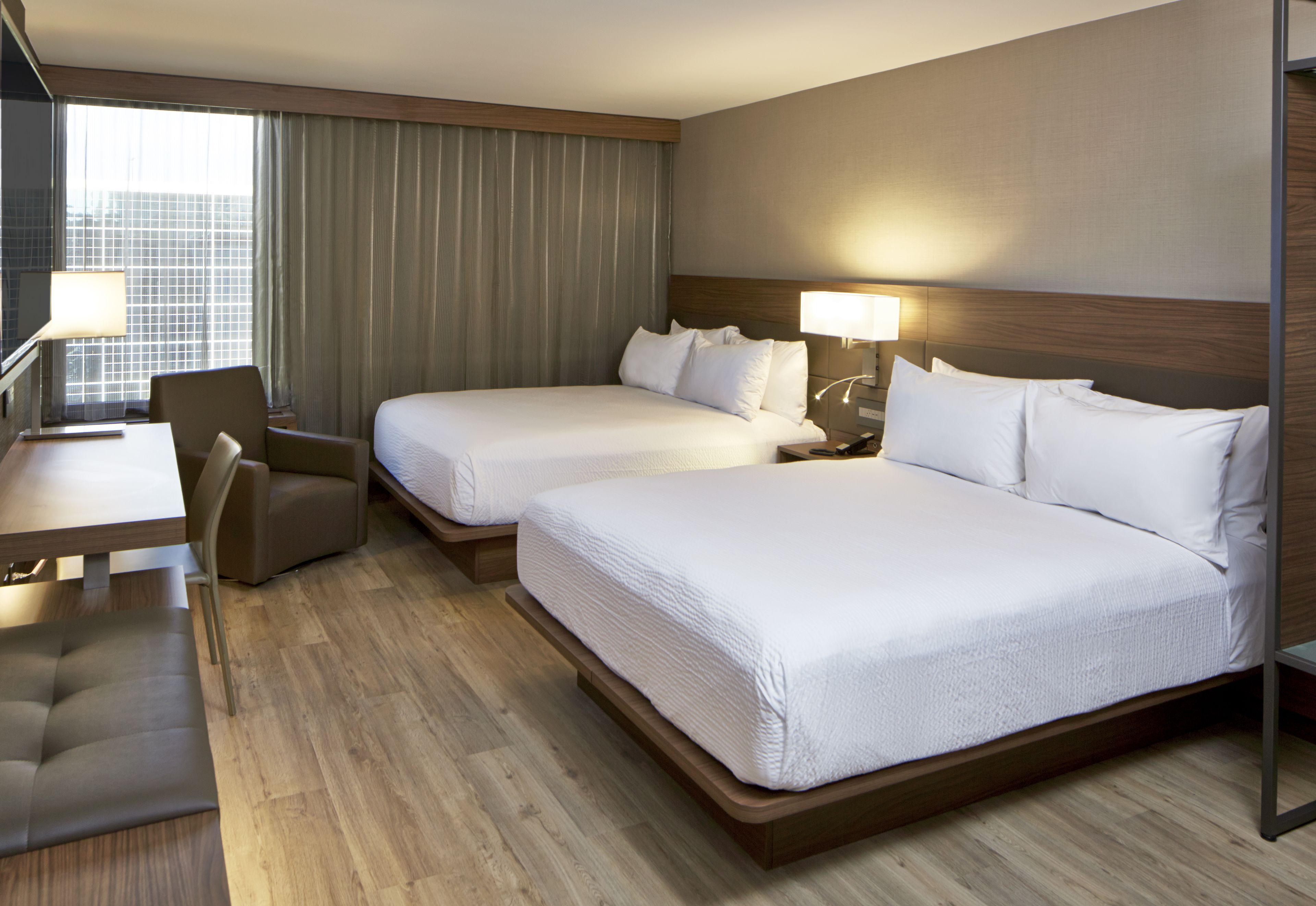 A hotel room with two beds, a desk, a chair, and a lamp.