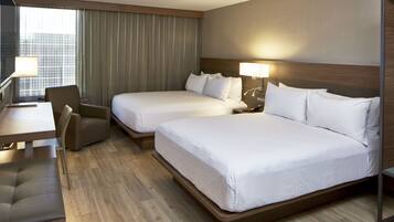 A hotel room with two beds, a desk, a chair, and a lamp.