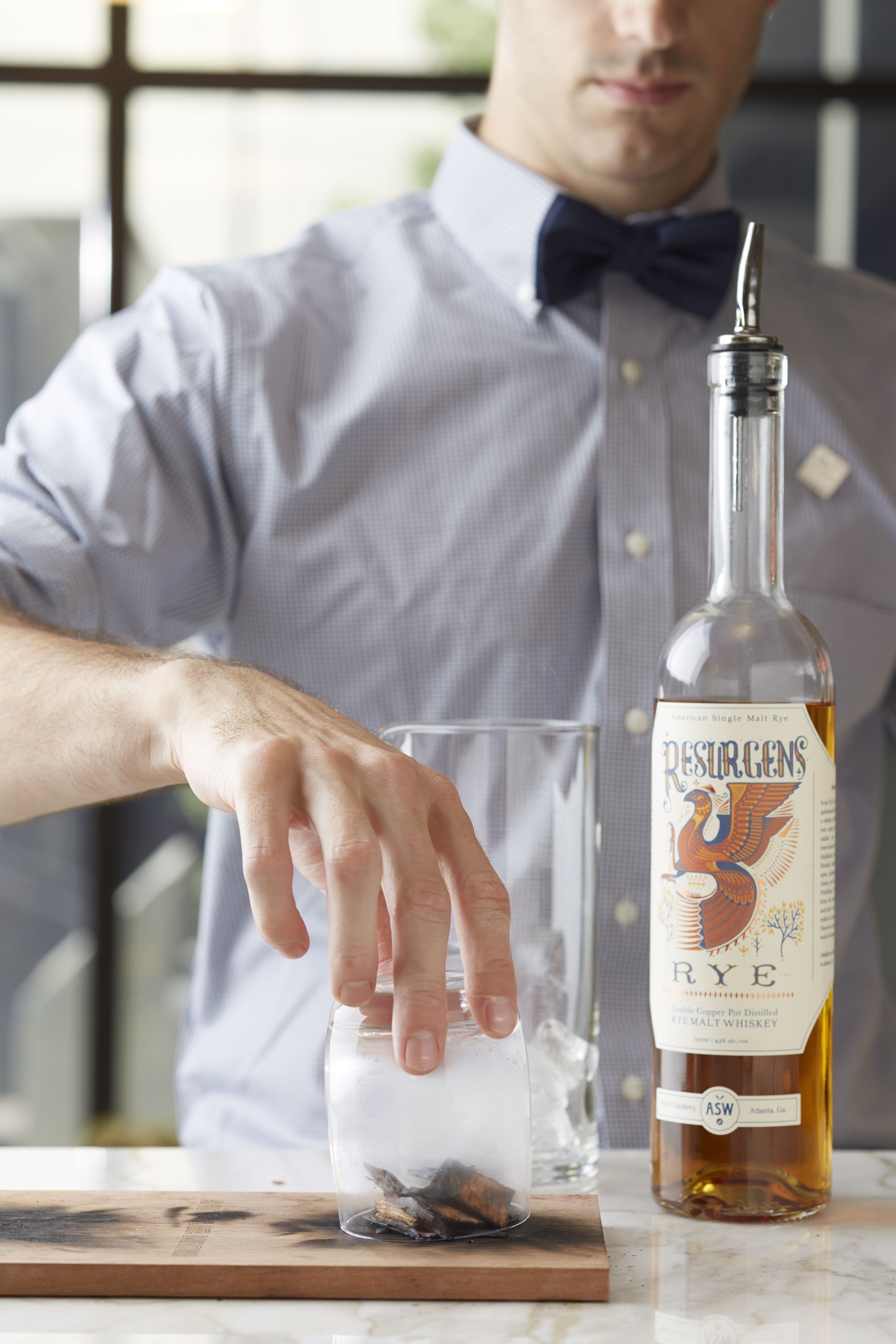 A person pouring a drink from a bottle labeled "Resurgens Rye" into a glass.
