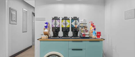 A coffee station with three coffee dispensers labeled 'Hot Water,' 'Regular Coffee,' and 'Decaf Coffee,' along with a hand soap dispenser and a bottle of lotion.