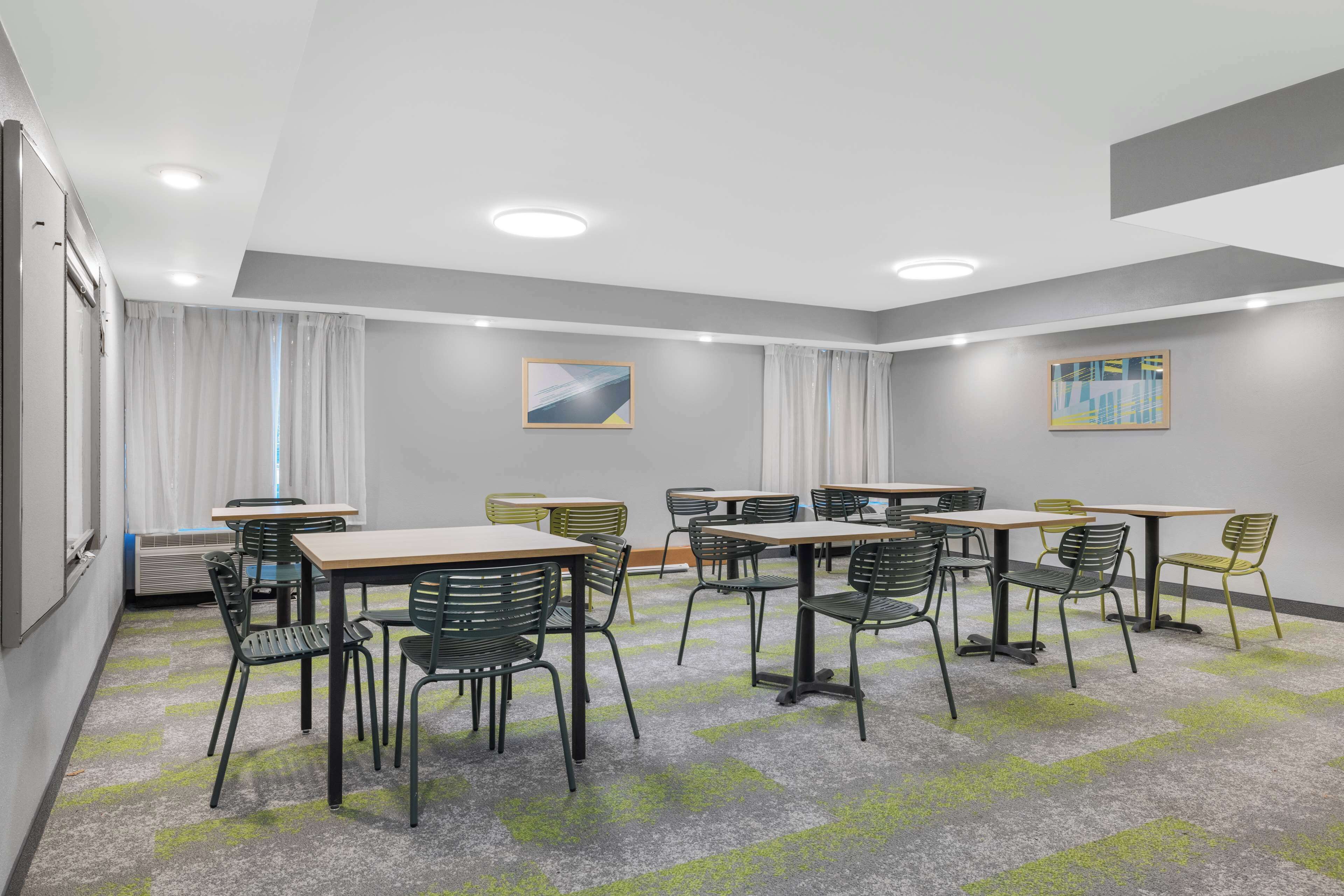 Ett konferensrum med bord och stolar, en projektorduk och ett stort fönster med gardiner.