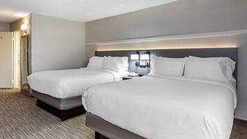 A hotel room with two beds, a bedside table with a lamp, and a door.
