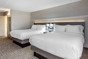 A hotel room with two beds, a bedside table with a lamp, and a door.