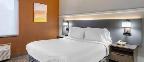 A hotel room with a large bed, bedside tables, a nightstand, a wall-mounted lamp, and a window with blinds.
