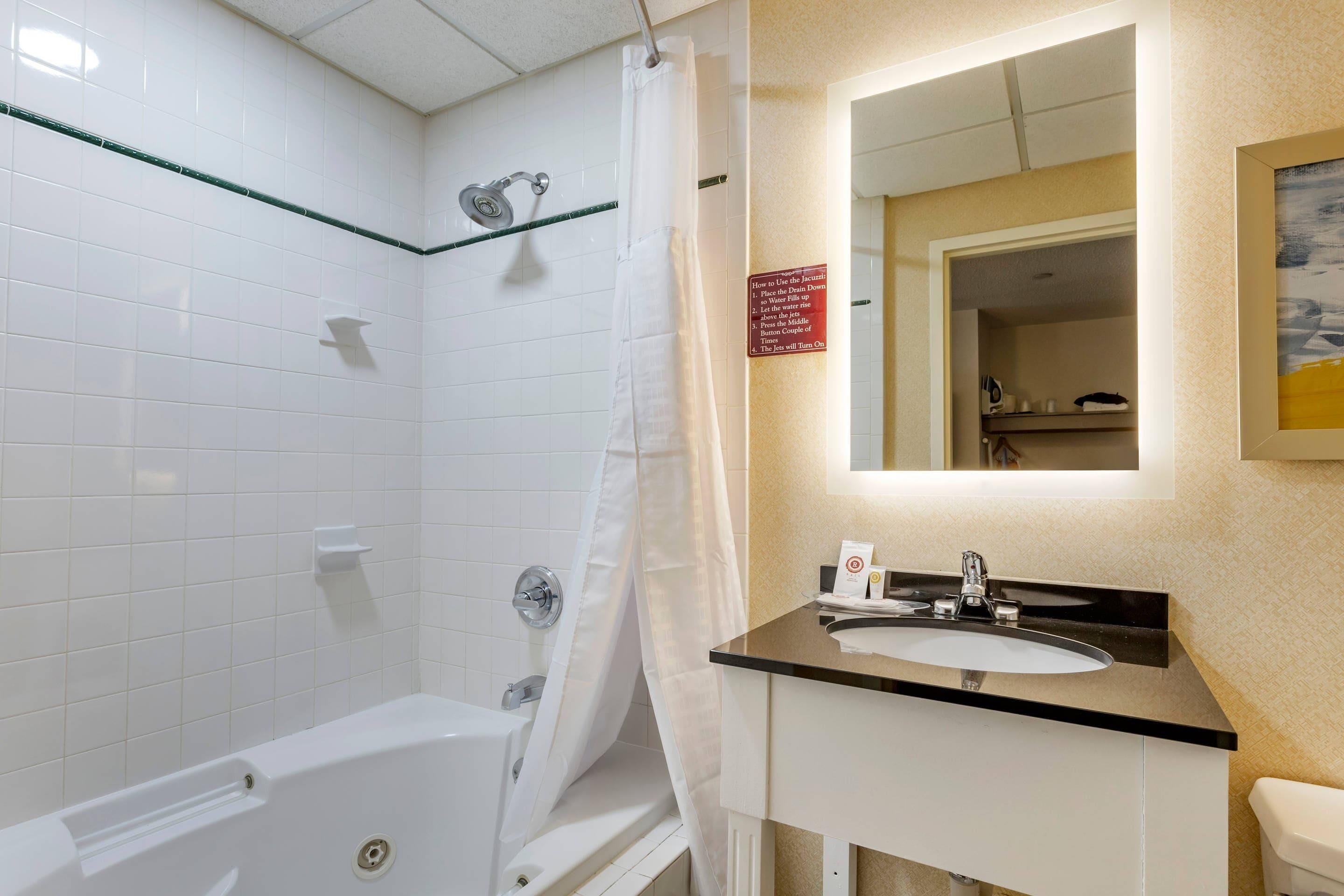 A bathroom with a bathtub, a shower curtain, a sink with a mirror, and a sign on the wall.