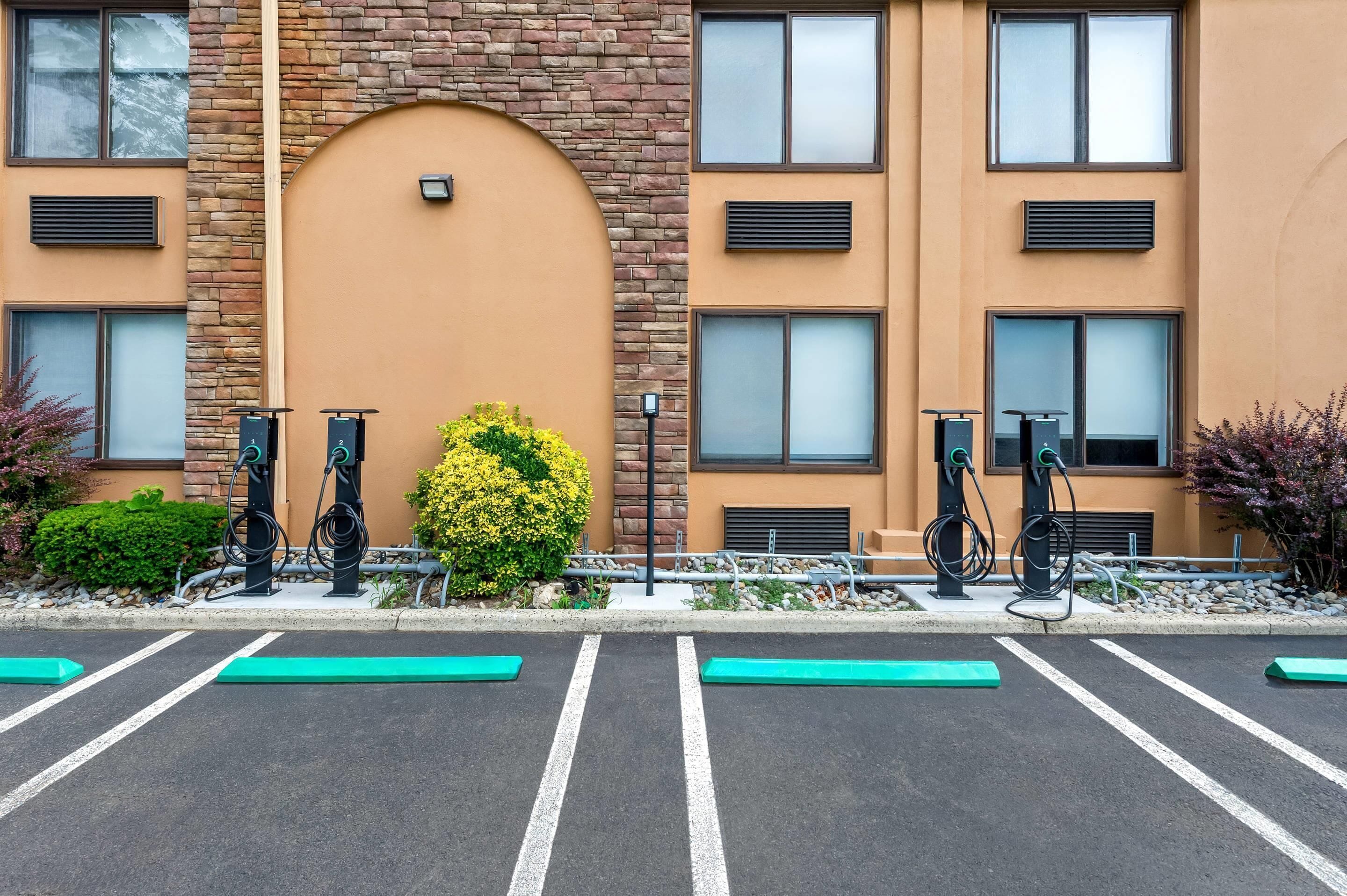 A parking lot with electric vehicle charging stations, a brick building with large windows, and a small bush.