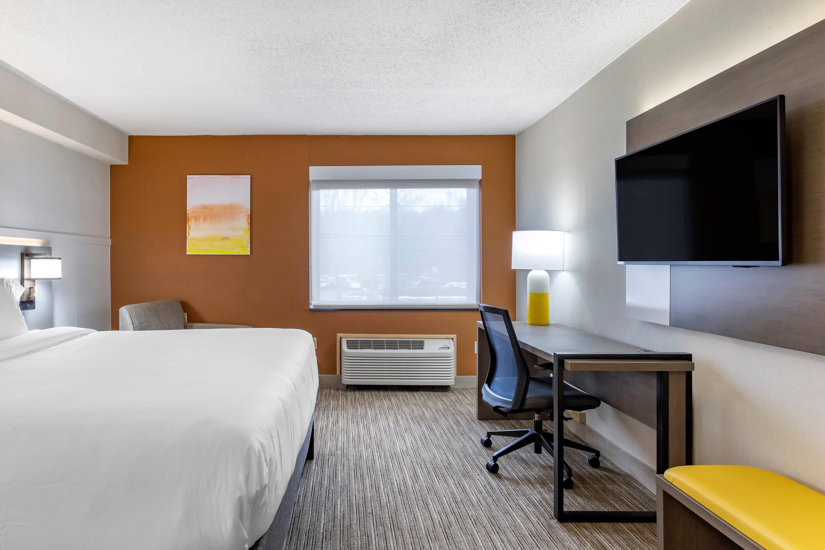 Een hotelkamer met een bed, bureau, stoel, televisie en kunst aan de muur.
