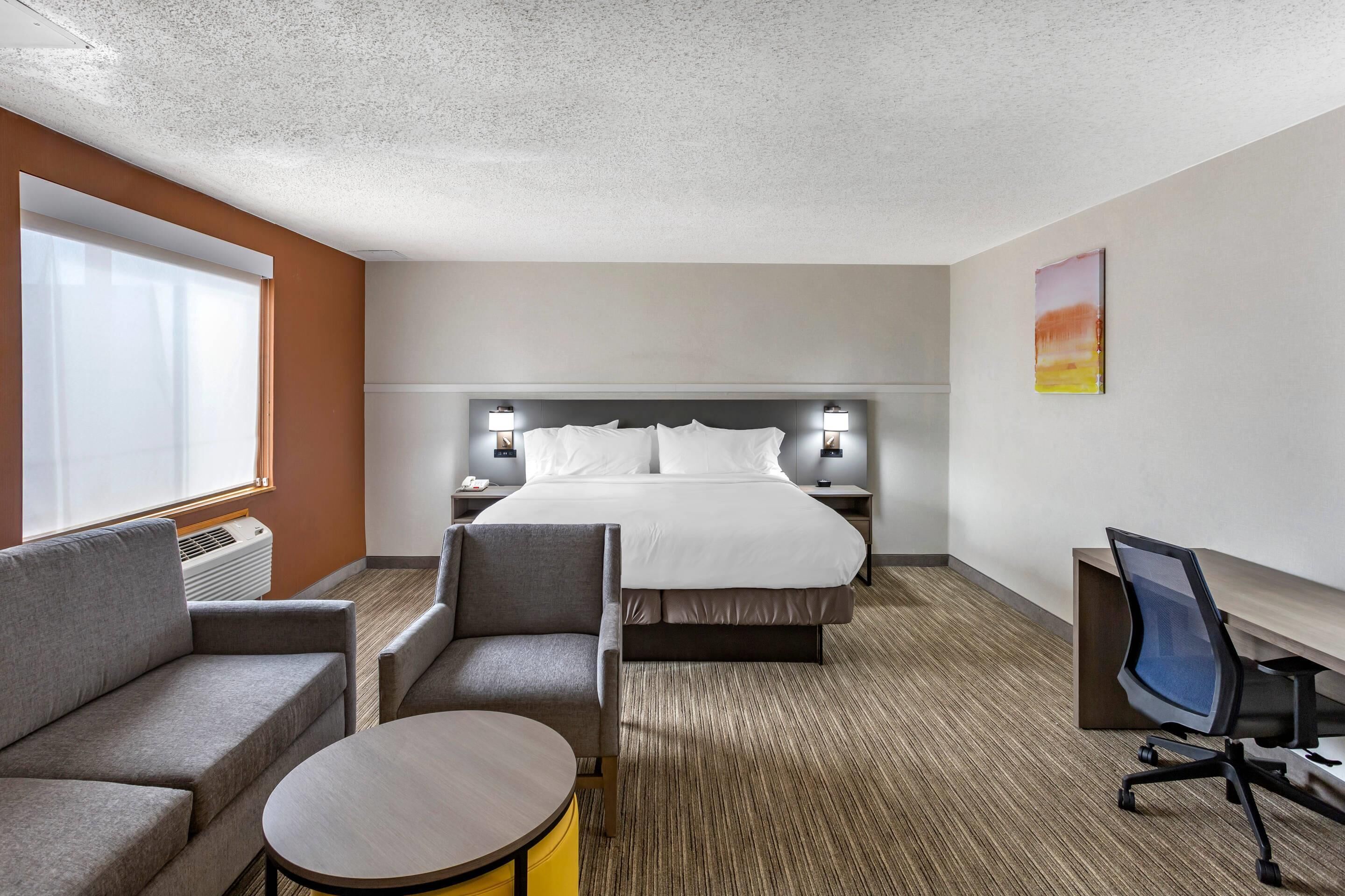 A hotel room with a bed, a sofa, a small round table, a desk with a chair, and a TV.