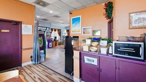 Un hall de hotel con un cubo de basura morado, un refrigerador y un microondas sobre una encimera.