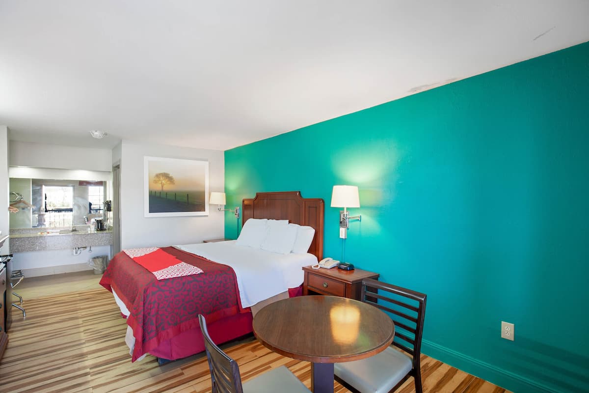A hotel room with a bed, bedside table, chair, and a round table.
