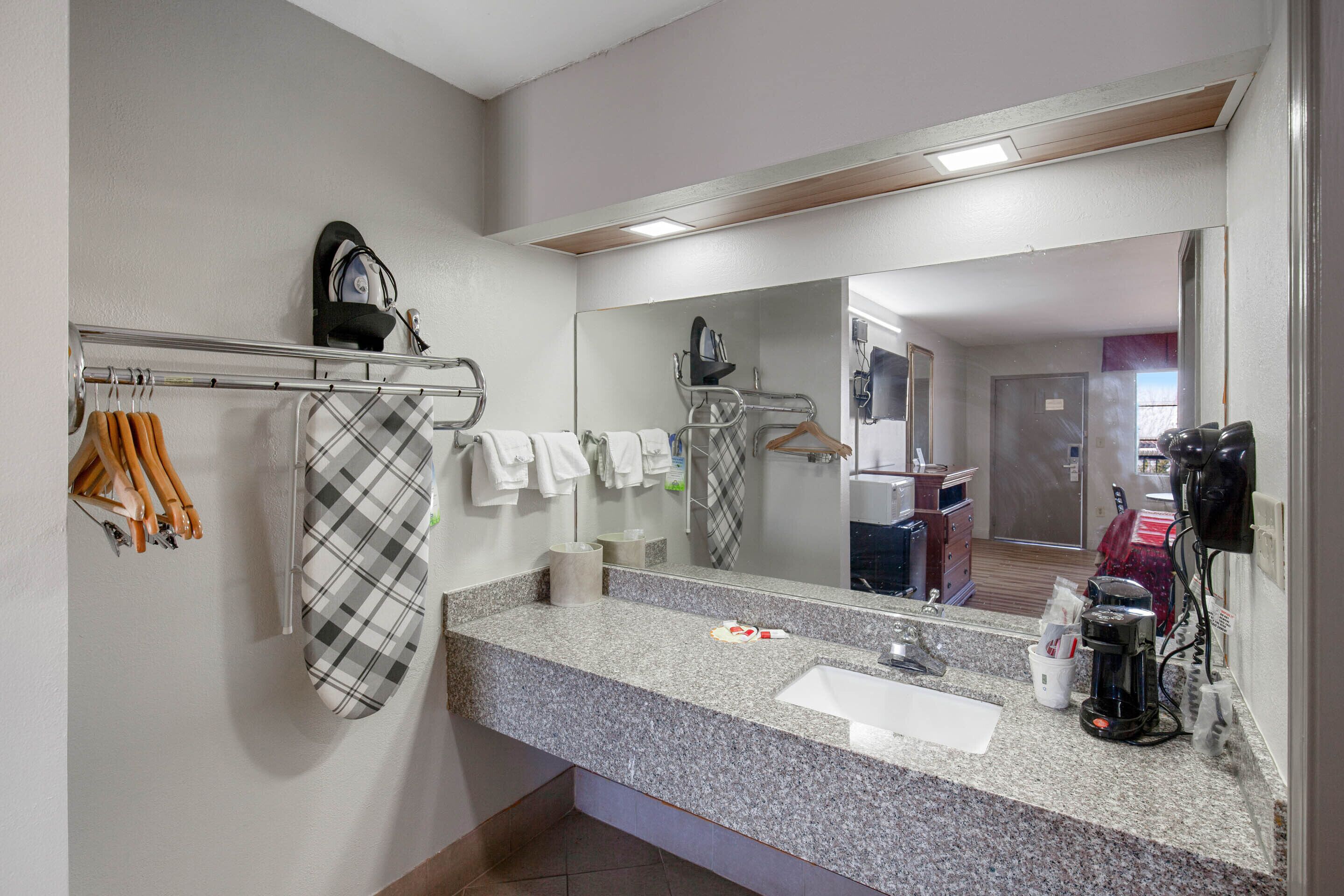 A bathroom with a granite countertop, a sink, a mirror, and a towel rack with multiple towels.