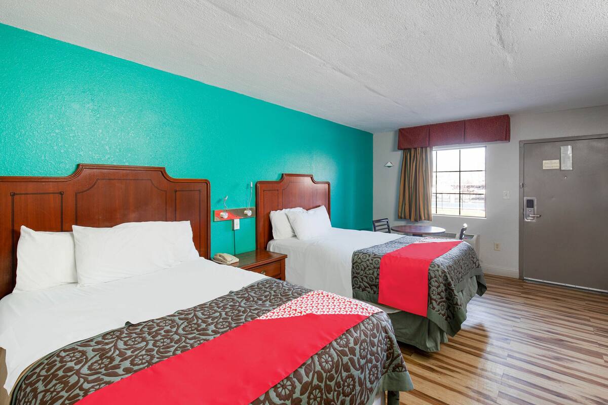 A hotel room with two beds, a window with curtains, a door, and a wooden floor.