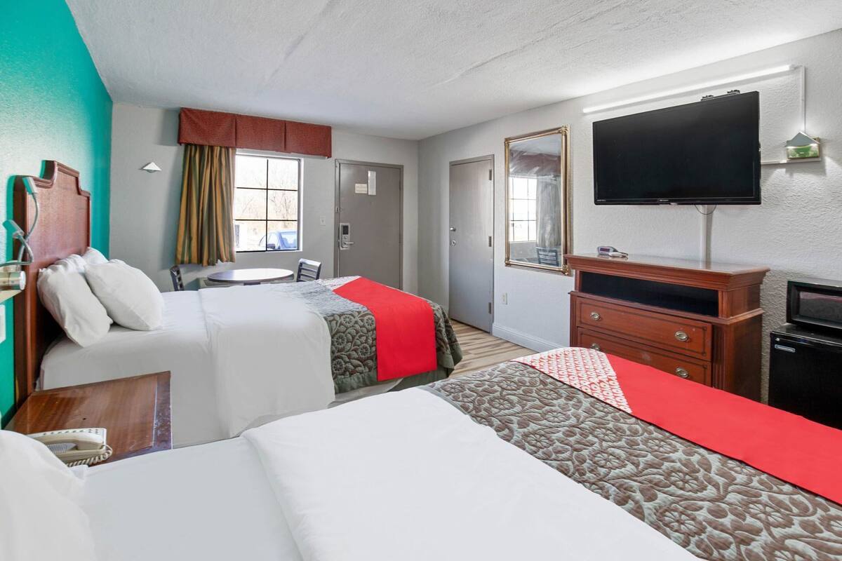 A hotel room with two beds, a desk, a television, a dresser, and a mirror.