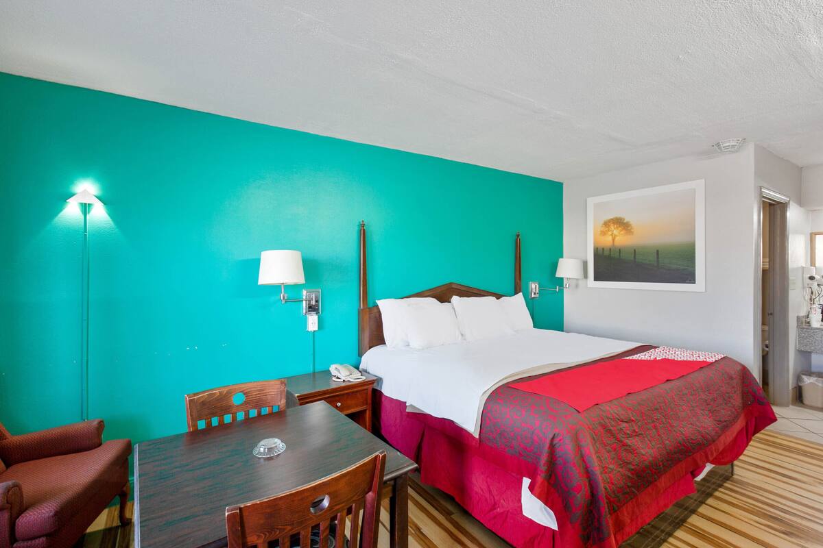 A hotel room with a bed, a desk, a chair, and a painting on the wall.