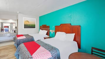 A hotel room with two beds, a wooden headboard, a teal accent wall, a painting, and a small table.