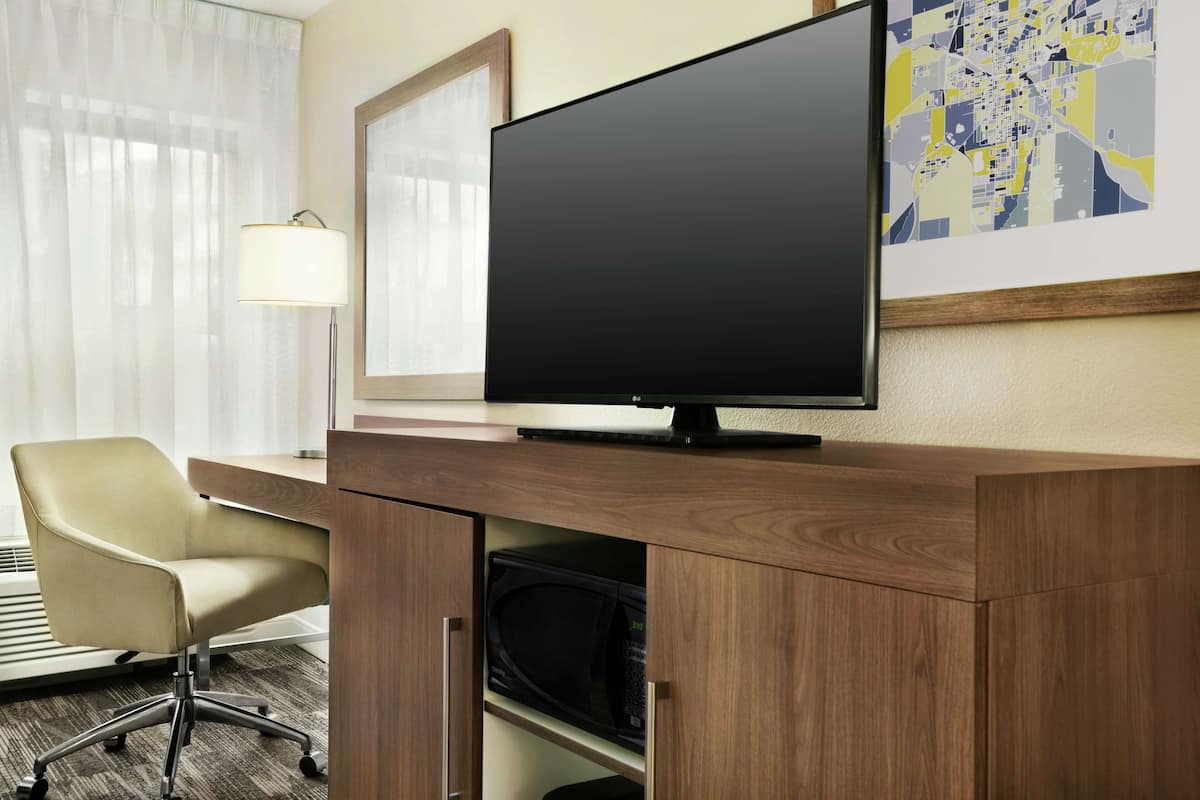 A hotel room with a wooden desk, a television, a chair, and a map on the wall.