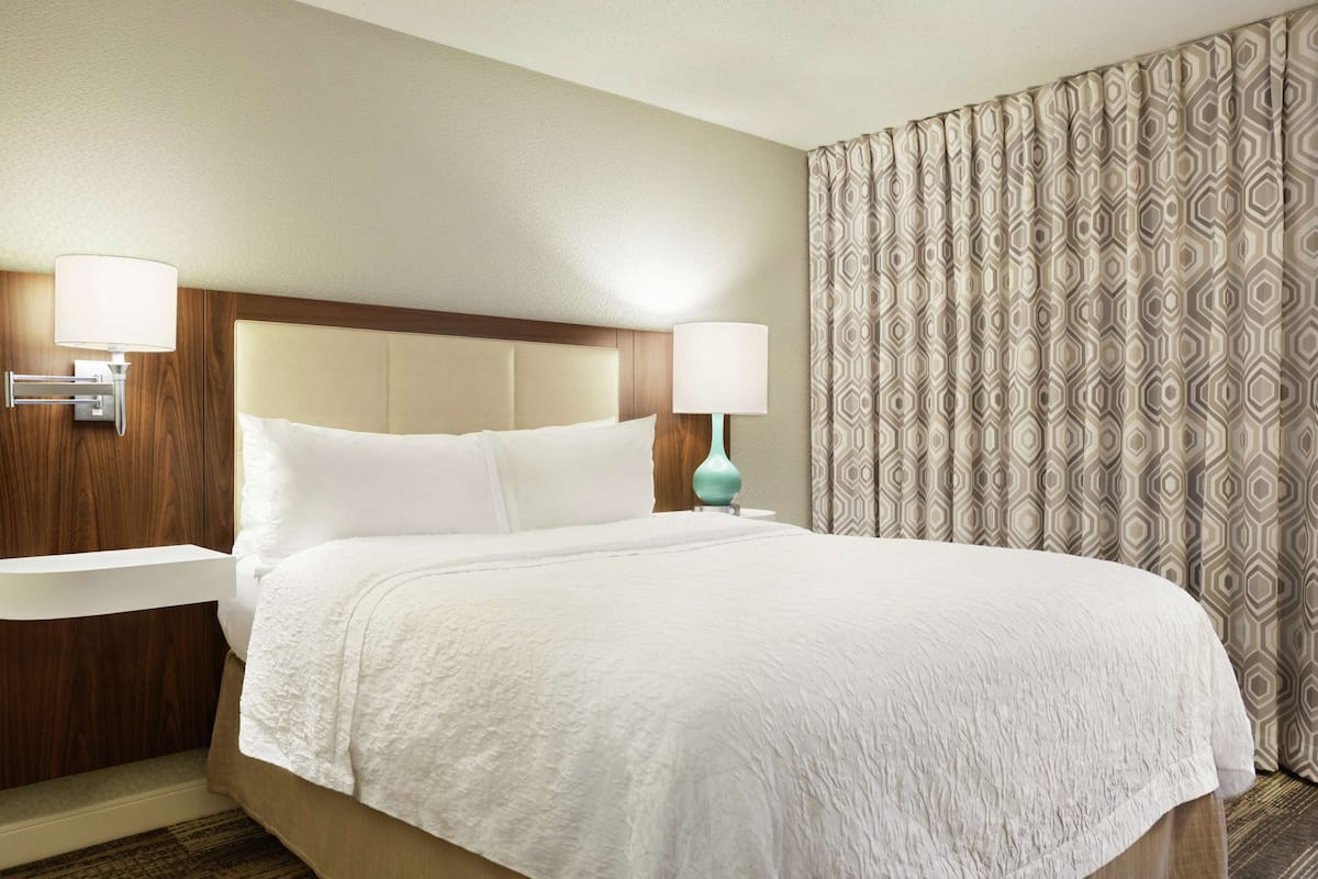 A hotel room with a large bed, two bedside tables, a nightstand, and a patterned curtain.