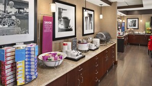 Zona de recepción de un hotel con un mostrador que exhibe diferentes alimentos y un cartel que anuncia un punto de venta de aperitivos.