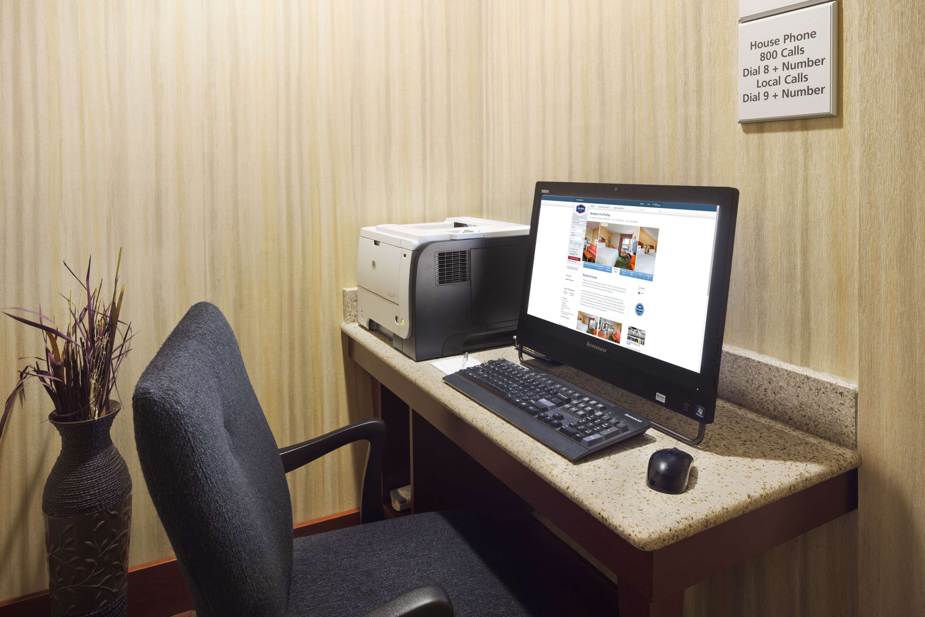 A hotel reception desk with a computer, printer, and a vase of dried plants.