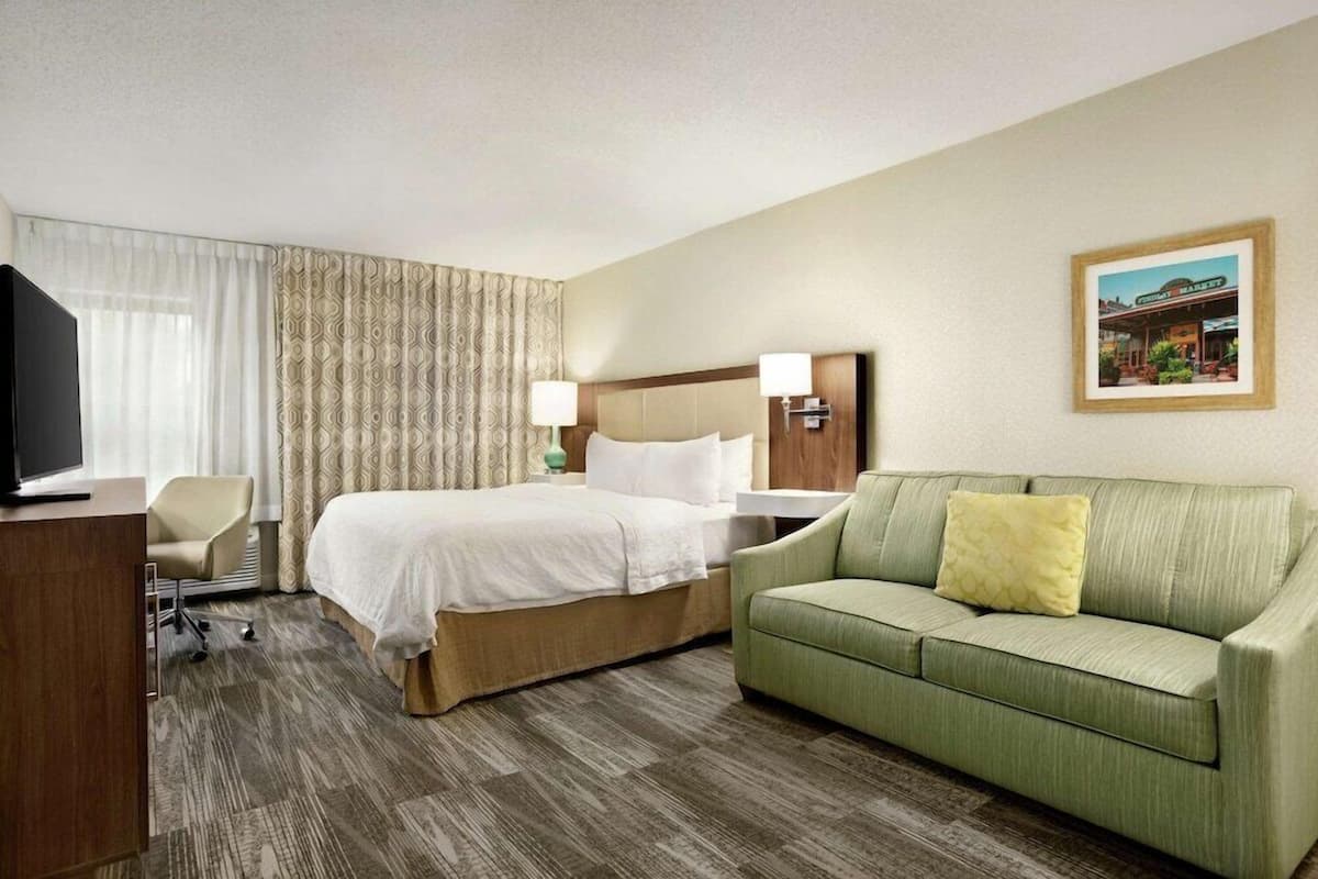 A hotel room with a bed, a green sofa, a desk with a TV, and a window with curtains.